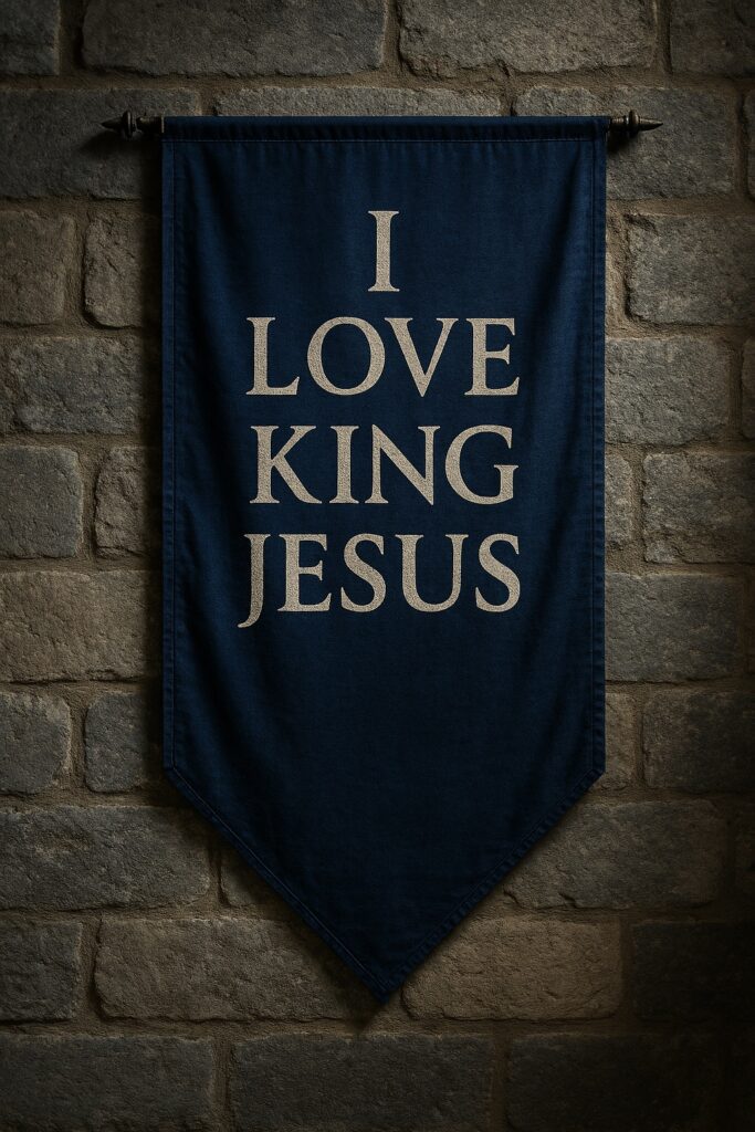 A dark blue banner hangs against a stone wall, displaying the words “I Love King Jesus” in bold light lettering beneath a decorative hanging rod.
